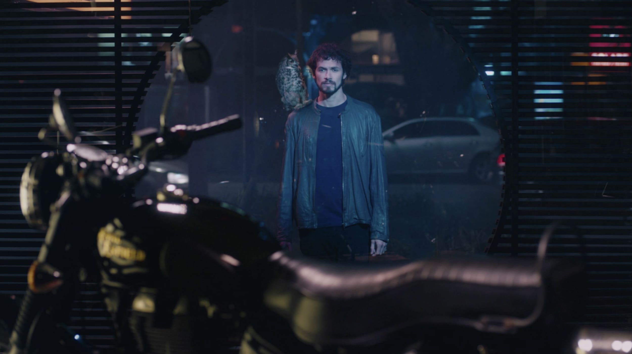 Hombre con un búho en el hombro, parado frente a una vidriera donde hay una moto.