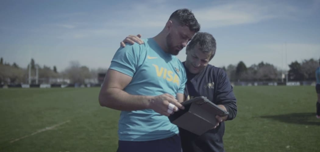 Javier Ortega Desio, jugador de los Los Pumas, junto con uno de los entrenadores del equipo mirando una tablet y hablando.